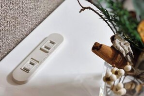 Une prise électrique blanche dotée d’un port USB, un objet en bois et un vase en verre contenant des baies blanches.