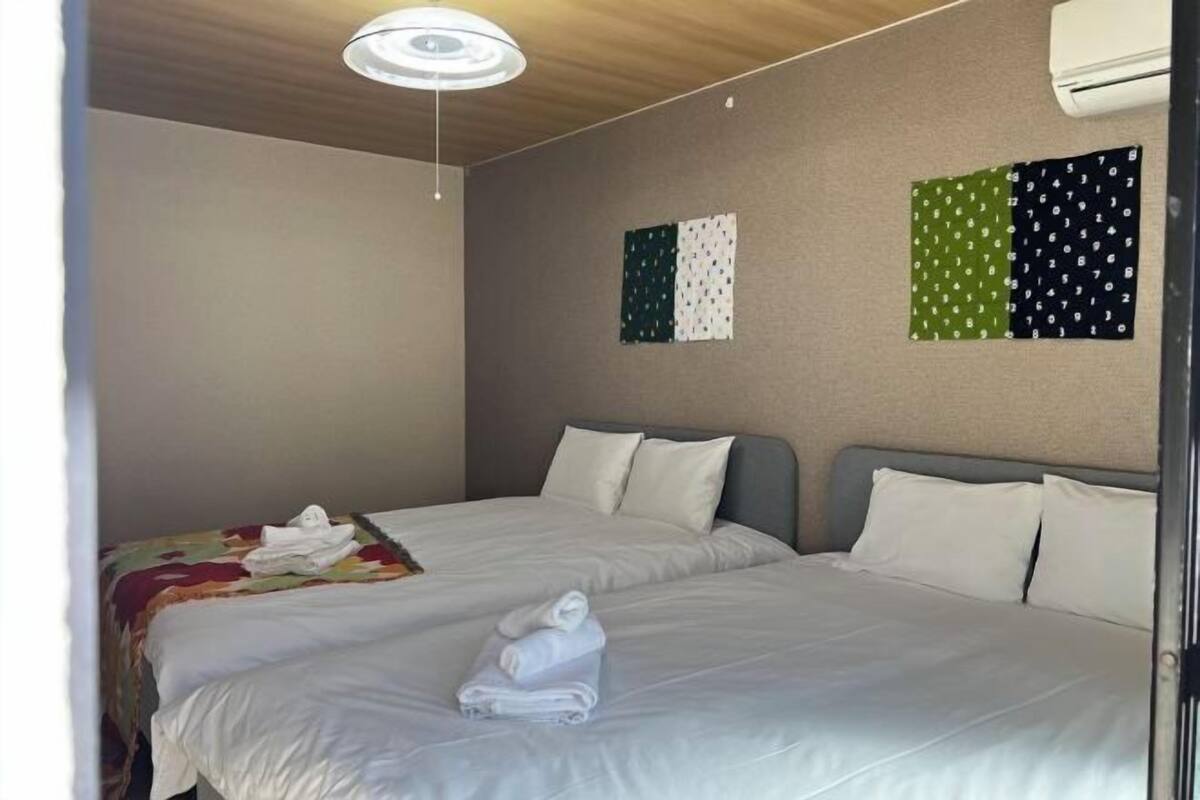 A hotel room with two beds, a ceiling light, and a wall with patterned flags.