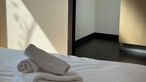 A neatly made bed with folded white towels, a wooden floor, and a door leading to another room. - Rest Collection Fushimi-Inari Kyoto (Kyoto)