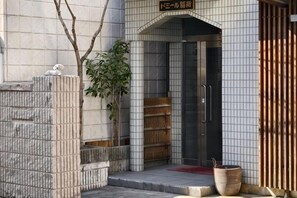 Una entrada de edificio con fachada de azulejos, una puerta de madera y una planta en maceta.