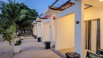 A hotel corridor with palm trees, trash bins, and a covered walkway.