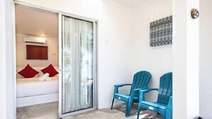 A room with a sliding glass door leading to a balcony, a white sofa with red cushions, and two blue chairs. - Coral Reef Holidays (Tioman)