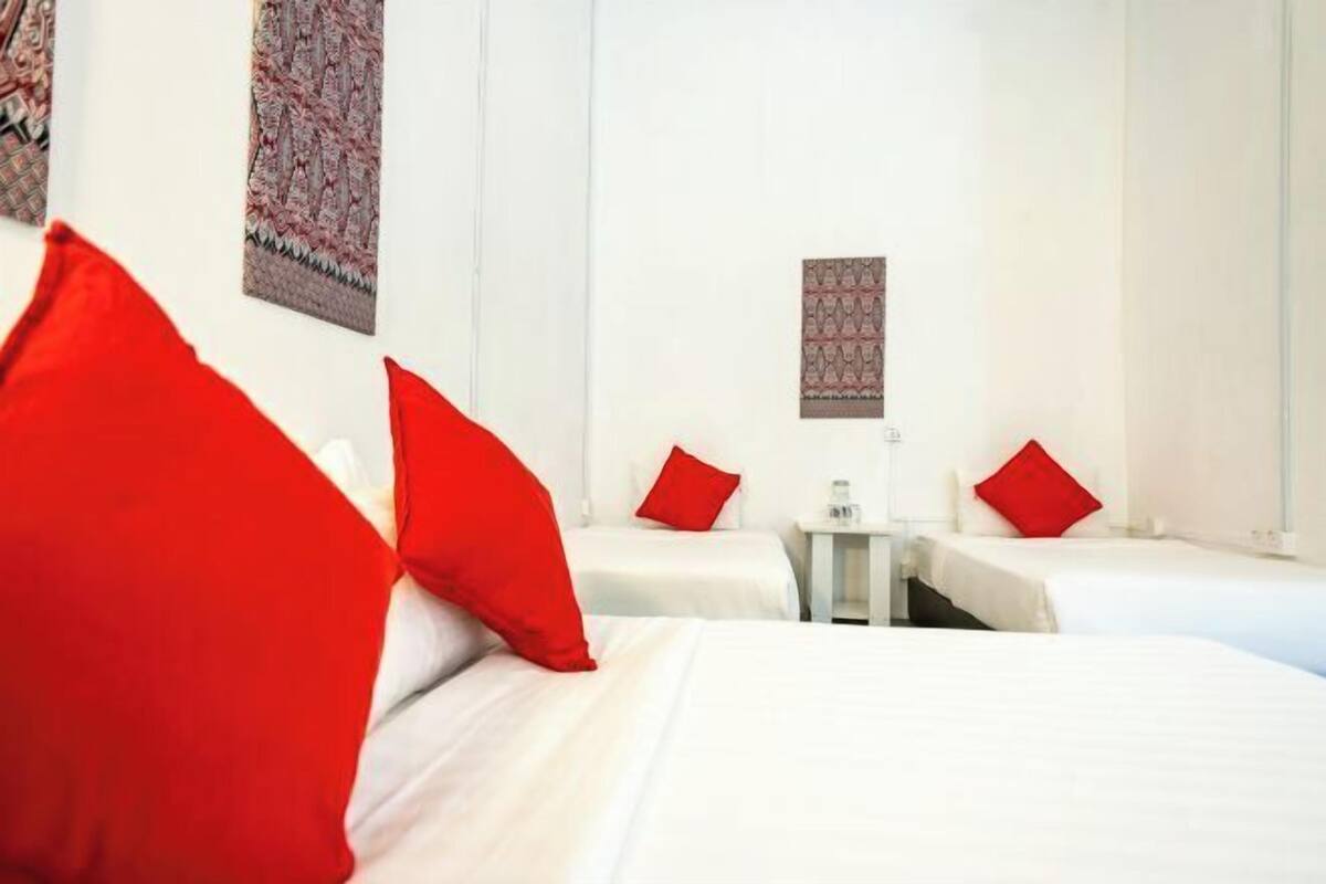 Une chambre d’hôtel avec deux lits, des oreillers rouges, une petite table et une œuvre d’art accrochée au mur.