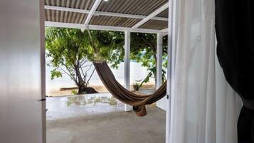 A hammock hanging under a white ceiling, a concrete floor, and a tree visible through a doorway.