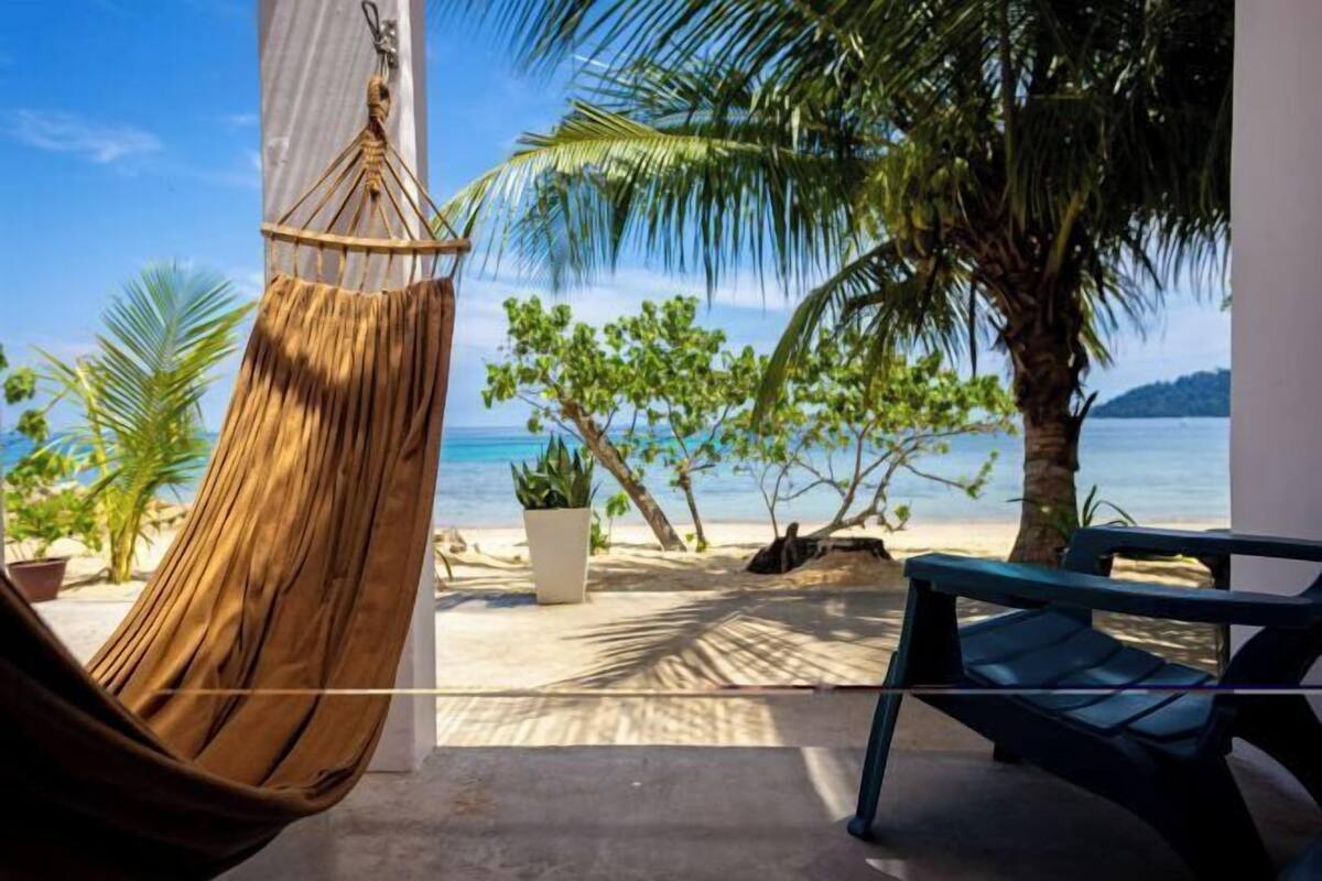 Un hamac, une chaise de plage et une vue sur l’océan, avec des palmiers en toile de fond.