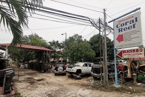 Un letrero anuncia Coral Reef, un bar de playa, y vehículos estacionados en un área de estacionamiento con suelo de tierra.