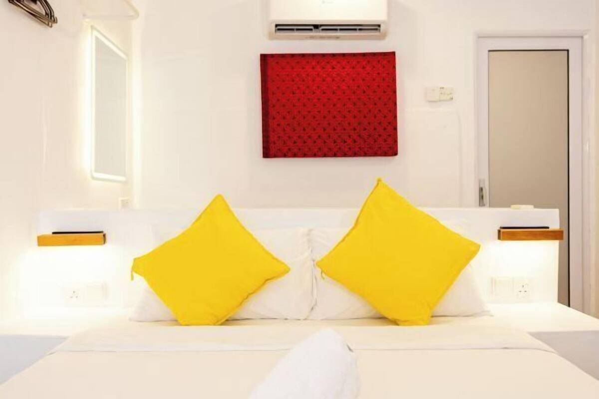 Une chambre d’hôtel avec un lit, deux oreillers jaunes, une décoration murale rouge à motifs et une porte blanche.