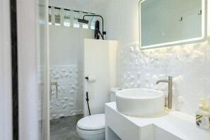 Un baño con lavamanos, espejo y retrete blancos.