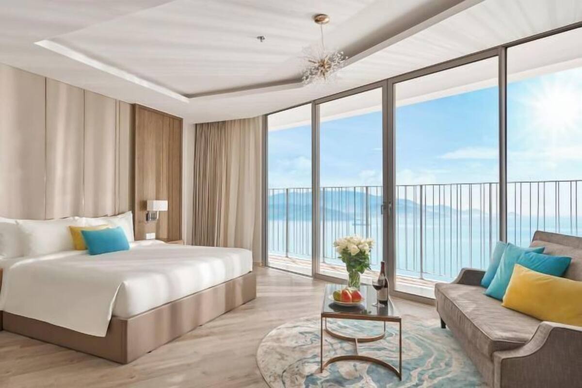 A hotel room with a large bed, a sofa, a coffee table, and a view of the sea.