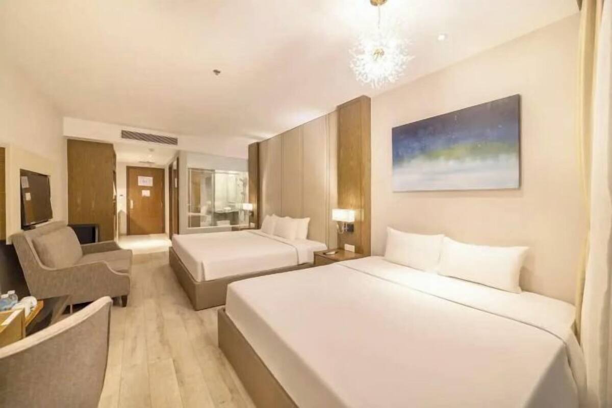 A hotel room with two beds, a sofa, a TV, and a painting on the wall.