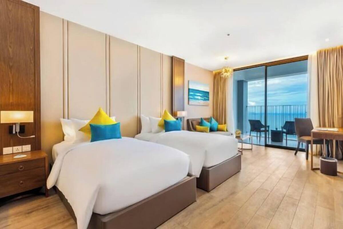 A hotel room with two beds, a desk, a chair, and a balcony with a view.