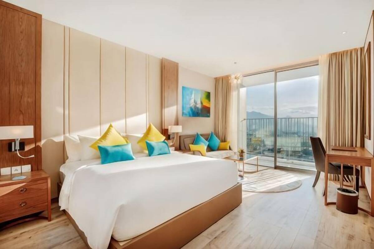 A modern hotel room with a large bed, a desk, and a view of the city.