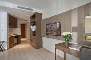 Une chambre d’hôtel avec un meuble en bois, un téléviseur fixé au mur, un vase avec des fleurs sur une table et une affiche accrochée au mur.
