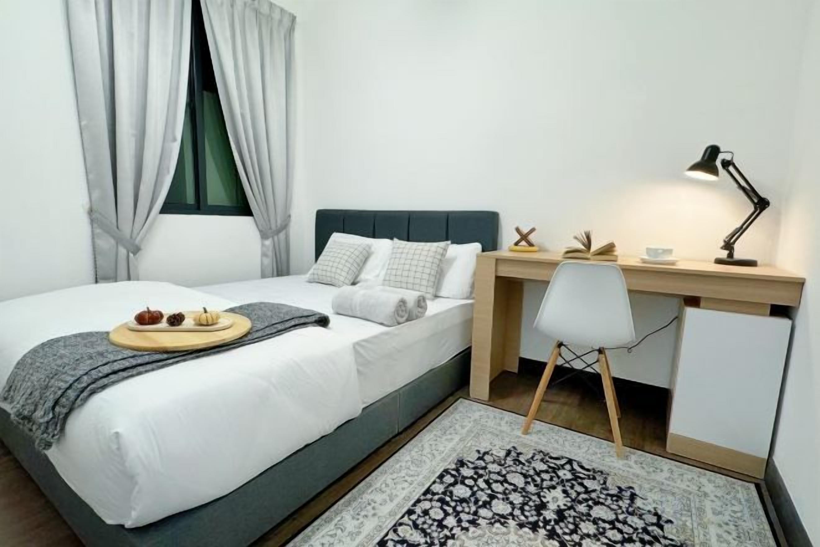 Un dormitorio ordenado con cama, escritorio, silla y una mesita de noche con lámpara.