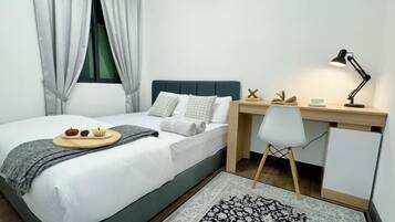 Un dormitorio ordenado con cama, escritorio, silla y una mesita de noche con lámpara.