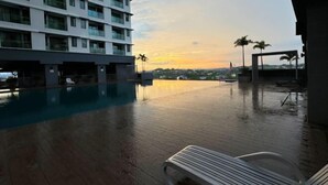 Ein Poolbereich mit Blick auf ein Hochhaus und Palmen bei Sonnenuntergang.