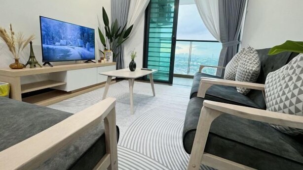 Ein modernes Wohnzimmer mit Flachbildfernseher, Couchtisch, einer Couch mit gemusterten Kissen und einem großen Fenster mit Vorhängen.