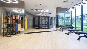 A modern gym with wooden flooring, exercise equipment, and a glass enclosure for weights. - The KH Arena Cam ranh Nha trang Beachside (Cam Ranh)