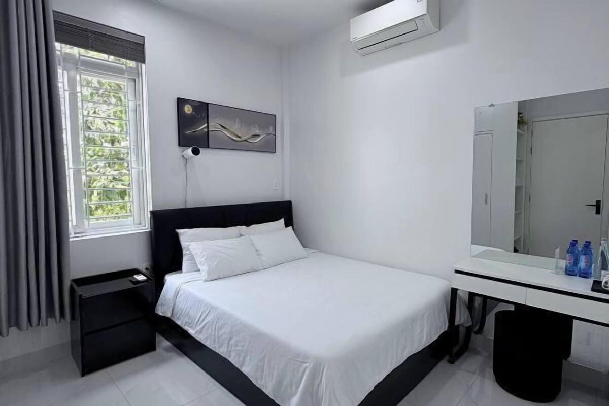 A bedroom with a bed, a bedside table, a mirror, and a window with curtains.
