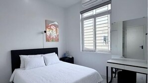 A bedroom with a bed, a bedside table, a mirror, and a window with blinds. - Niki Homestay (Hue)