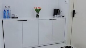 A white cabinet with a vase of flowers, two bottles, and a coffee maker. - Niki Homestay (Hue)