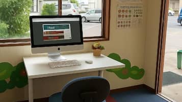 Un escritorio con un monitor, teclado y ratón, una planta pequeña y carteles educativos en la pared.