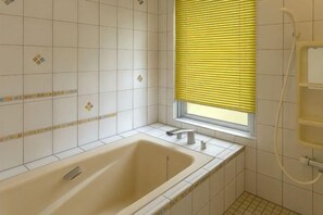 A bathroom with a bathtub, a window with blinds, and a shower area. - Mt.Fuji Homestay Leoya (Fuji)