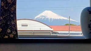 A view of Mount Fuji through a window, with a building featuring a red roof in the foreground. - Mt.Fuji Homestay Leoya (Fuji)