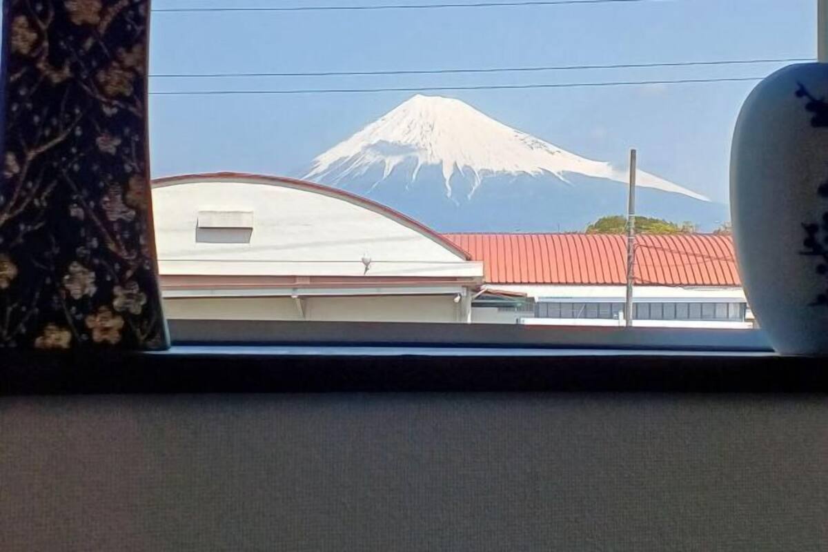 A view of Mount Fuji through a window, with a building featuring a red roof in the foreground.