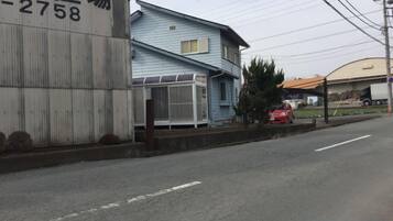 A street with a blue house, a large white building with a sign, and a parked red car.