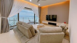 A modern living room with a sofa, TV, and balcony with a view. - Seafront Country Garden Danga Bay by Lions Bay (Johor Bahru)