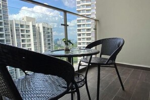A balcony with two wicker chairs and a small table, overlooking a cityscape with high-rise buildings. - Seafront Country Garden Danga Bay by Lions Bay (Johor Bahru)