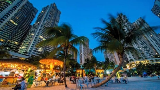 A beachside area with high-rise buildings, palm trees, and outdoor seating for dining. - Seafront Country Garden Danga Bay by Lions Bay (Johor Bahru)