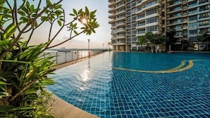 A swimming pool with a tiled floor, surrounded by greenery and a tall building in the background. - Seafront Country Garden Danga Bay by Lions Bay (Johor Bahru)
