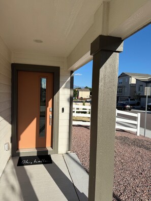 A residential entrance with a door, a doormat, and a clear view of the driveway and neighboring houses.