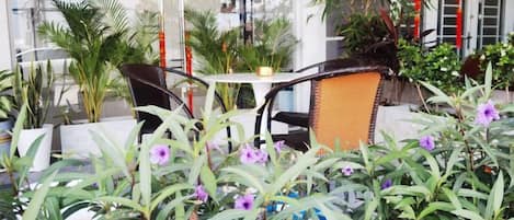 An outdoor seating area with tables and chairs, surrounded by potted plants and flowers.