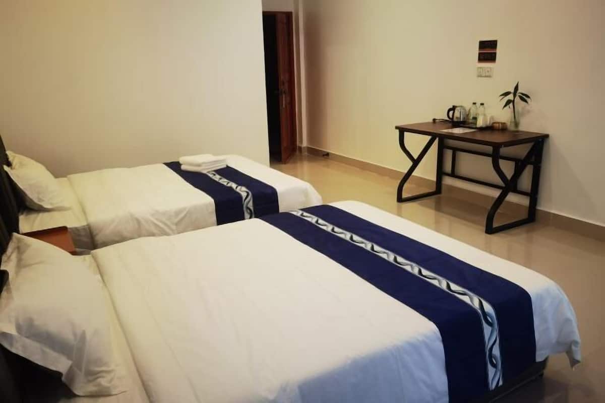 A hotel room with two beds, a small table with a plant, and a door in the background.