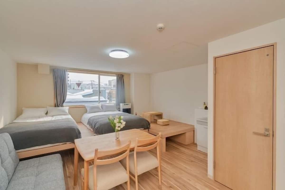 A compact hotel room with two beds, a dining table, and a small kitchenette.