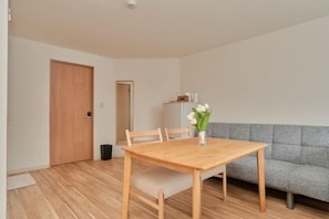 A dining area with a wooden table, chairs, a vase with flowers, a grey sofa, and a wooden door. - The Stay Yuki (Otaru)