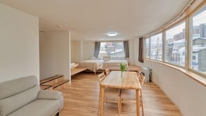 A modern apartment with a dining area, a sofa, a small table, and a view of the city through large windows. - The Stay Yuki (Otaru)
