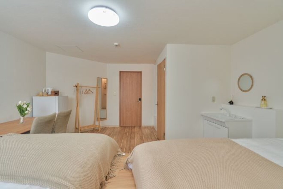 Hotellihuone, jossa on kaksi sänkyä, työpöytä, peili, vaatekaappi ja kylpyhuone.