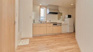A compact kitchen with wooden cabinets, a microwave, and a refrigerator. - The Stay Yuki (Otaru)