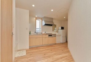 A compact kitchen with wooden flooring, a window, and a microwave. - The Stay Yuki (Otaru)