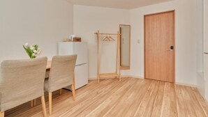A room with a wooden floor, a white wall, a wooden door, a small table with chairs, and a mirror. - The Stay Yuki (Otaru)