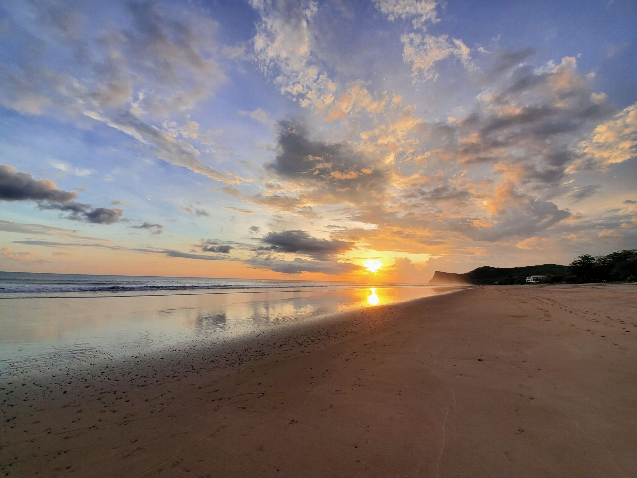 A beach with a sunset, calm sea, and a clear sky.