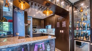 A modern bar area with a granite countertop, glass display cases with bottles, and a hanging light fixture.
