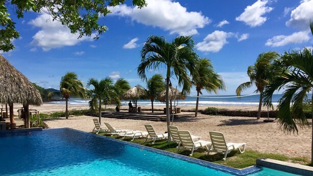A pool area with lounge chairs and a view of the beach.