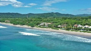 A coastal property with beachfront villas, clear turquoise waters, and a backdrop of green hills.