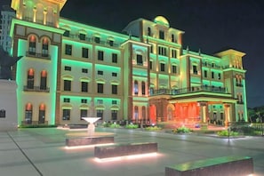 Un hôtel à plusieurs étages, doté d’une entrée imposante, d’une fontaine et d’une façade bien éclairée.