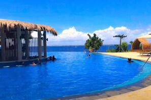 A swimming pool with a thatched-roof structure, a lounge area, and a view of the ocean. - Ocean Suites at One Pacific Residence - Mactan Newtown (Lapu-Lapu City)